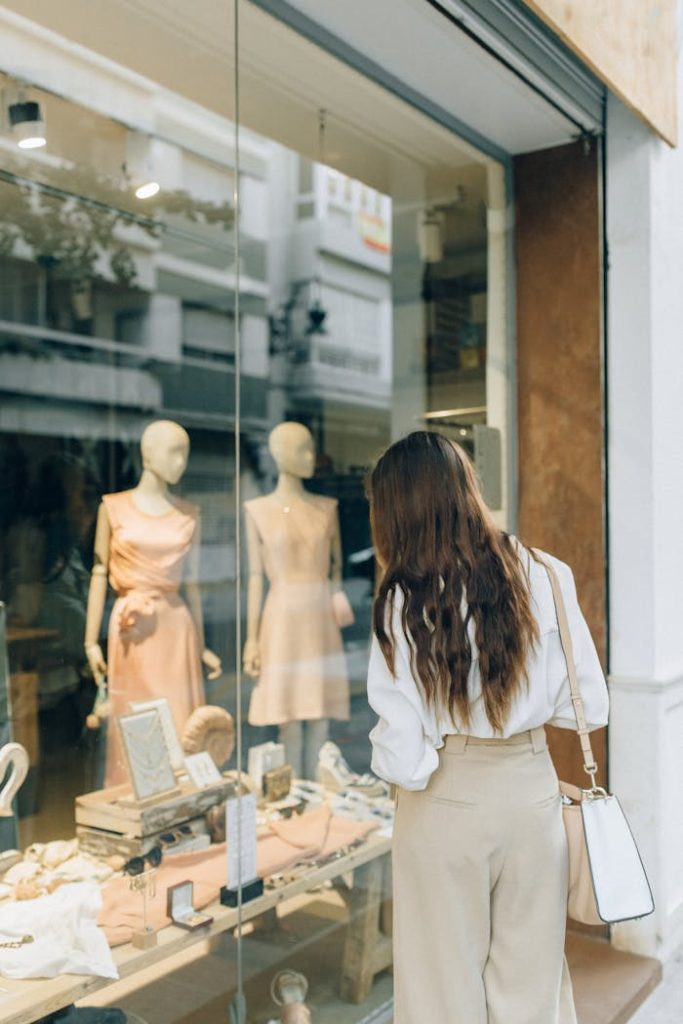 Woman with long hair window shopping in a stylish fashion store with elegant displays.