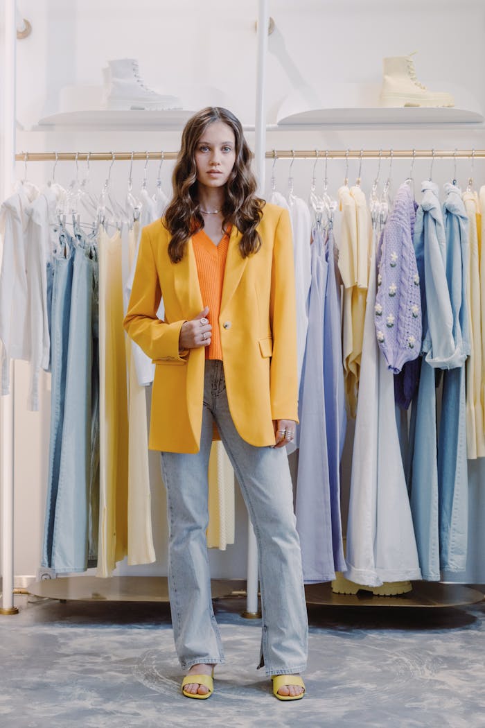 Chic fashion showcase with a woman in a vibrant yellow blazer posing amidst colorful clothing in a stylish boutique.